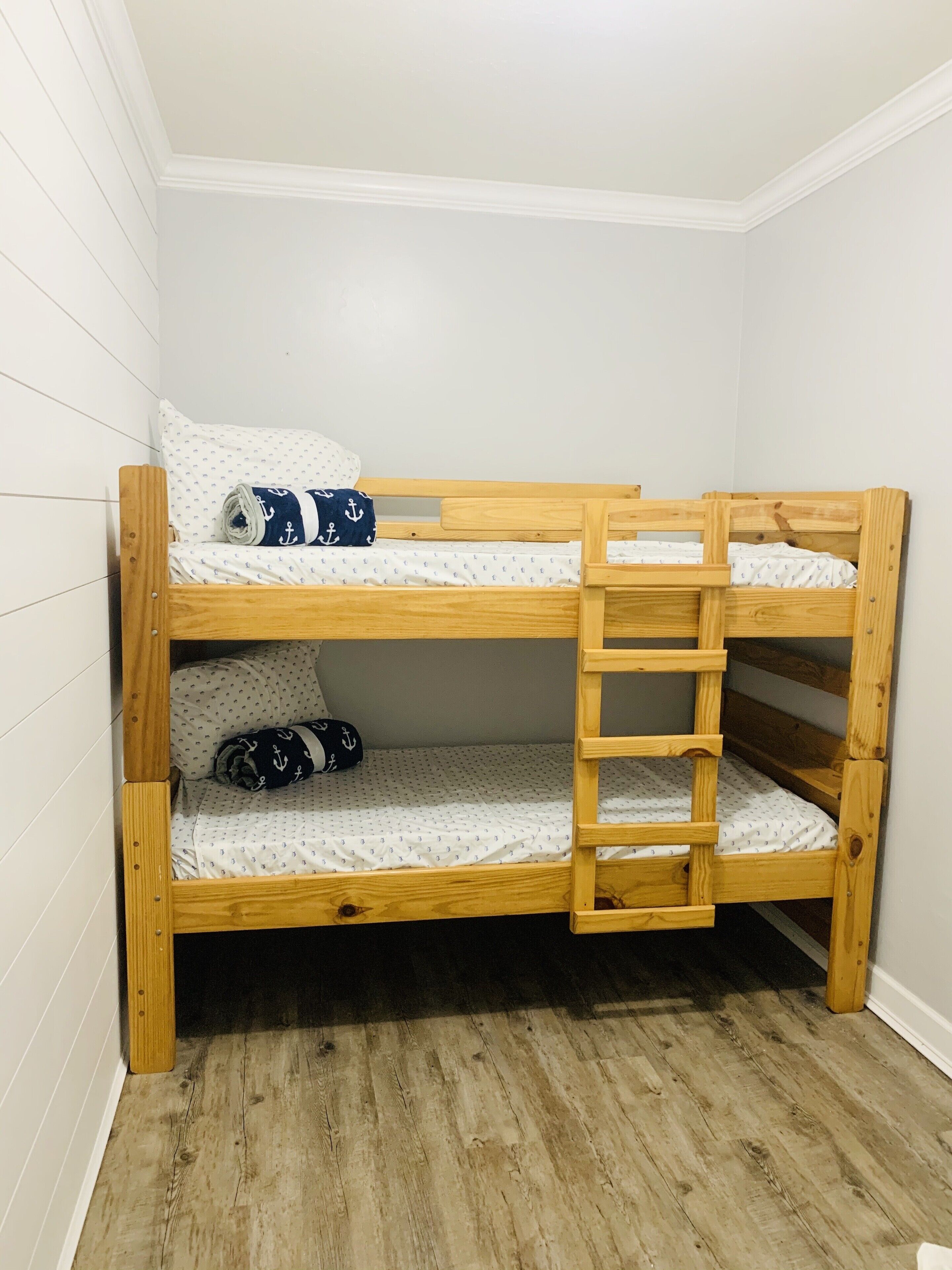 A bunk bed with a ladder, white walls, and wooden flooring.