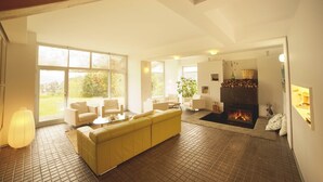 Amplia sala de estar con un sofá amarillo, una chimenea y ventanas grandes que ofrecen vistas al exterior.