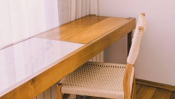 Un escritorio de madera con una silla trenzada en una habitación con suelo de madera y paredes blancas.