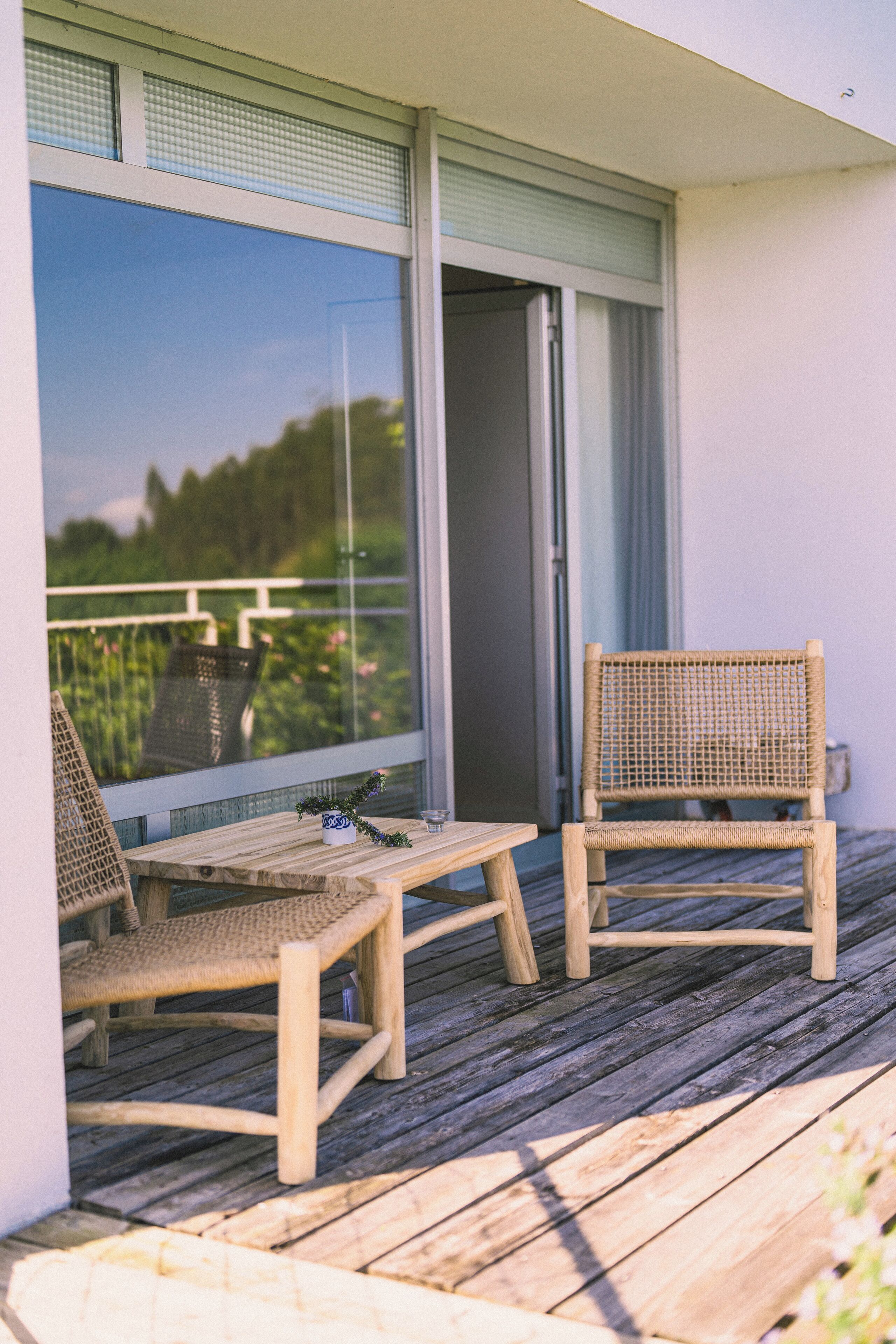 Un balcon avec deux fauteuils en osier et une petite table, donnant sur un jardin.