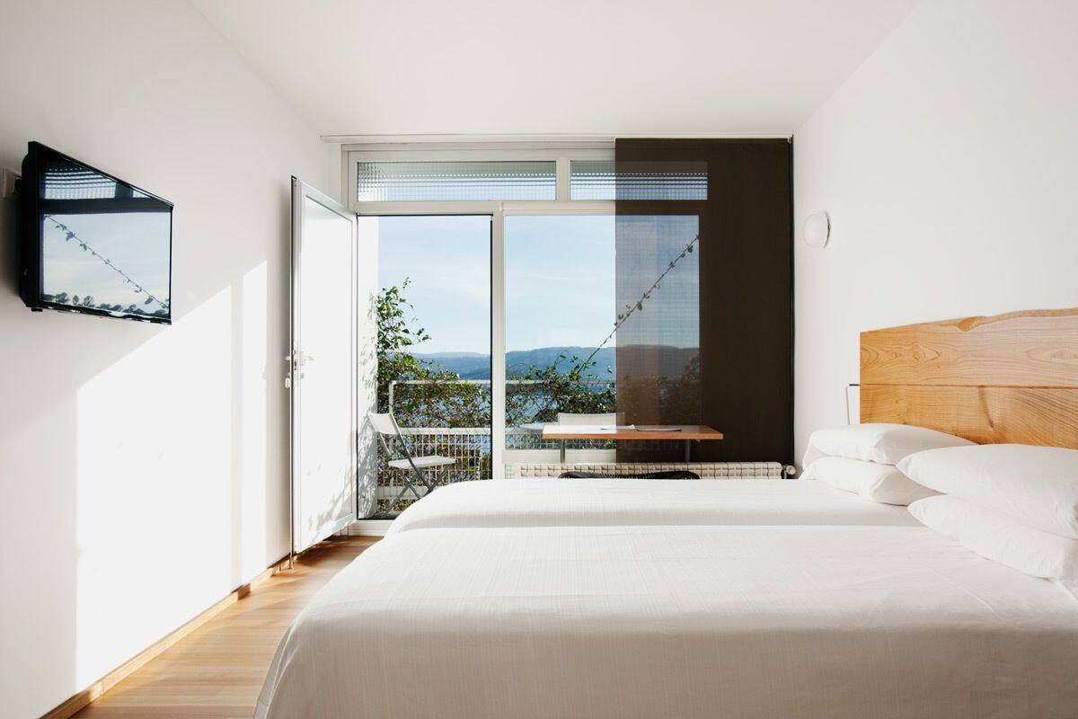 Quarto com cama grande, cabeceira de madeira, televisão na parede e varanda com vista para o exterior.