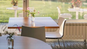 Un comedor con una mesa y sillas, una lámpara colgante y vistas a un jardín a través de amplios ventanales.
