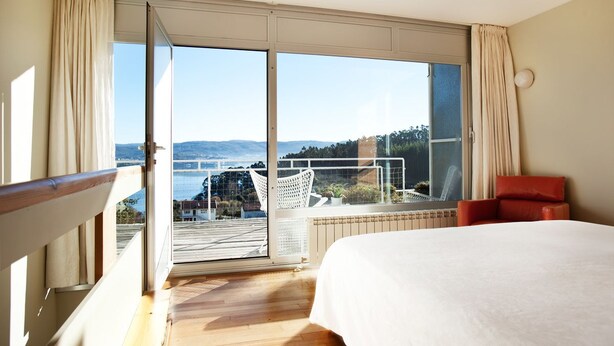 Una habitación de hotel con una cama grande, vistas al mar y un balcón con una silla.
