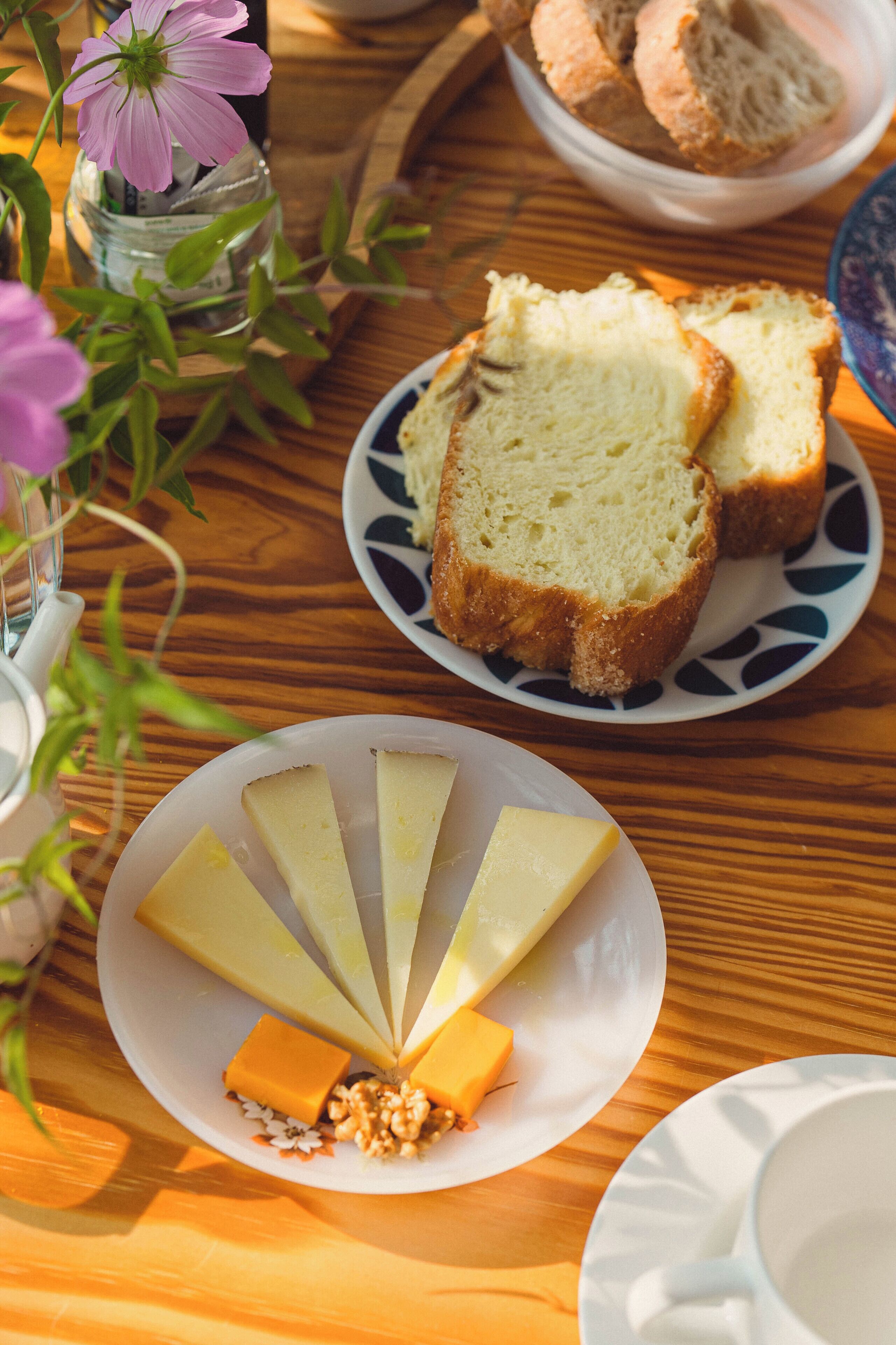 Ein Holztisch mit Käse, Brot und einer kleinen Vase mit einer Blume.