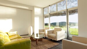 Una sala de estar moderna con una mesa de centro de vidrio, sillones color beige y un sofá amarillo.