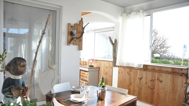 A dining area with a wooden table set for two, a bottle of wine, and a decorative squirrel statue. - Large T3 with terrace, sea view, 20 metres from the beach (NARBONNE PLAGE)
