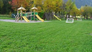 Un parque infantil con toboganes y estructuras para escalar, rodeado de árboles y montañas.