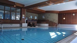 Una piscina con suelo de baldosas, vigas de madera y una pared de piedra.