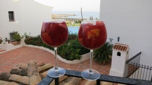 Two glasses of red beverage on a balcony overlooking a pool and ocean. - Cabopino (Marbella)