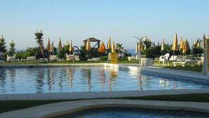 A pool area with lounge chairs and umbrellas, surrounded by palm trees and a clear sky. - Cabopino (Marbella)
