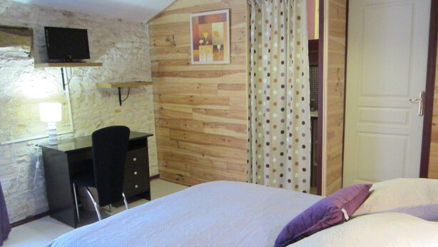 Une chambre à coucher comprenant un lit, un bureau, une chaise, un téléviseur fixé au mur, qui est en pierre, et une porte.