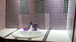 Une salle de bain avec un lavabo blanc, un porte-gobelet violet et des murs carrelés.