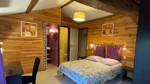 Une pièce chaleureuse avec un plafond en bois, un lit recouvert d’une literie à motifs floraux, un bureau avec une chaise et une petite table.