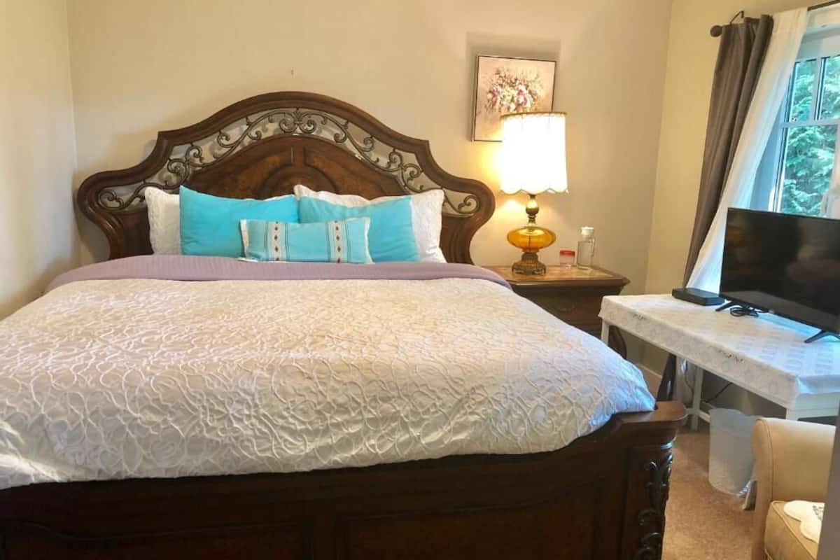 Una cama bien hecha con cabecera de madera, una mesita de noche con lámpara y un televisor sobre un mueble.