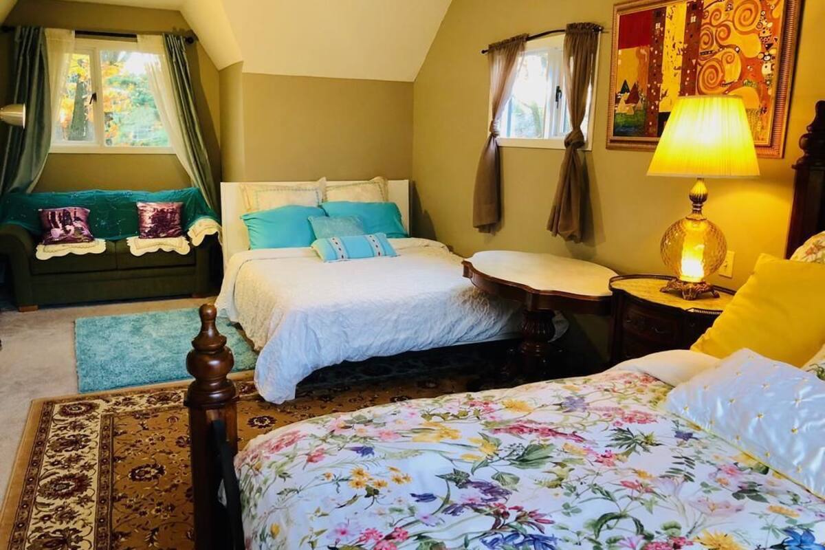 Un dormitorio con dos camas, una mesita de noche, una lámpara, un cuadro y una ventana con cortinas.