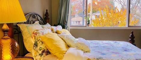 Ein Schlafzimmer mit Bett, Lampe und Blick auf Herbstlaub.