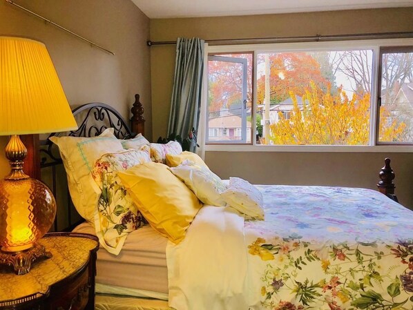 Un dormitorio con cama, lámpara y ventana con vista a follaje otoñal.