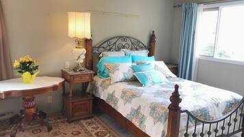 A bedroom with a bed, a nightstand, a lamp, a table with a vase of flowers, and a window with curtains.