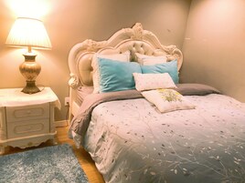 A bedroom with a classic white bed, a nightstand with a lamp, and a blue rug.