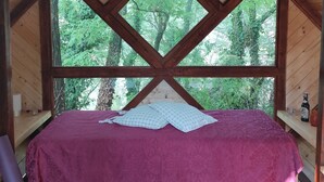 Una cabaña de madera con una cama, un ventanal y una botella en un estante.