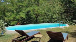 Una piscina rodeada de exuberante vegetación, con dos sillas de descanso y una mesita.