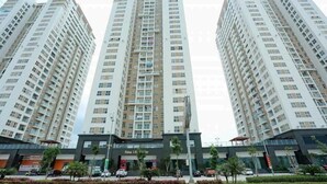 A high-rise residential building with multiple floors, a central entrance, and a commercial area with shops and vehicles. - Ha Long Pearl Apartment (Bai Chay)