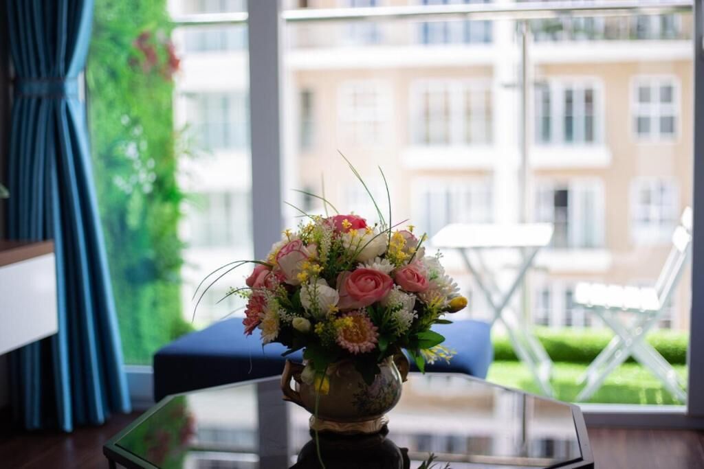 Una habitación con una mesa de vidrio, un florero con flores, una silla azul y vistas a edificios a través de grandes ventanales.