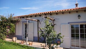 A house with a tiled roof, a pergola, and a garden with potted plants and flowers.