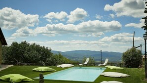 Une piscine avec vue sur les montagnes, entourée d’une pelouse verdoyante et de coussins blancs.