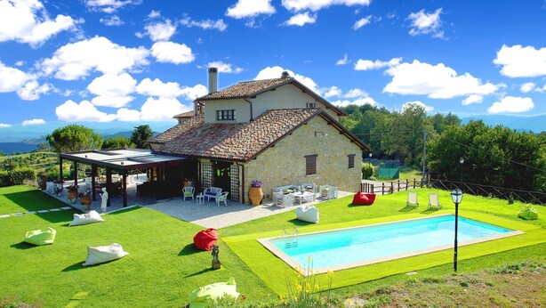 Une maison en pierre avec un toit en tuiles, une piscine et un espace salon extérieur.