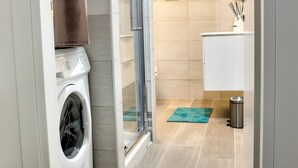 Une salle de bain moderne équipée d’un lave-linge, d’une cabine de douche en verre et d’une petite poubelle.