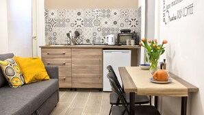 Une cuisine compacte avec un crédence décorée, une machine à café et un petit coin repas comprenant une table et des chaises.