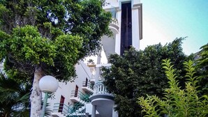 Un edificio bianco con una torre centrale, circondato da vegetazione lussureggiante e una scalinata che conduce all'ingresso.