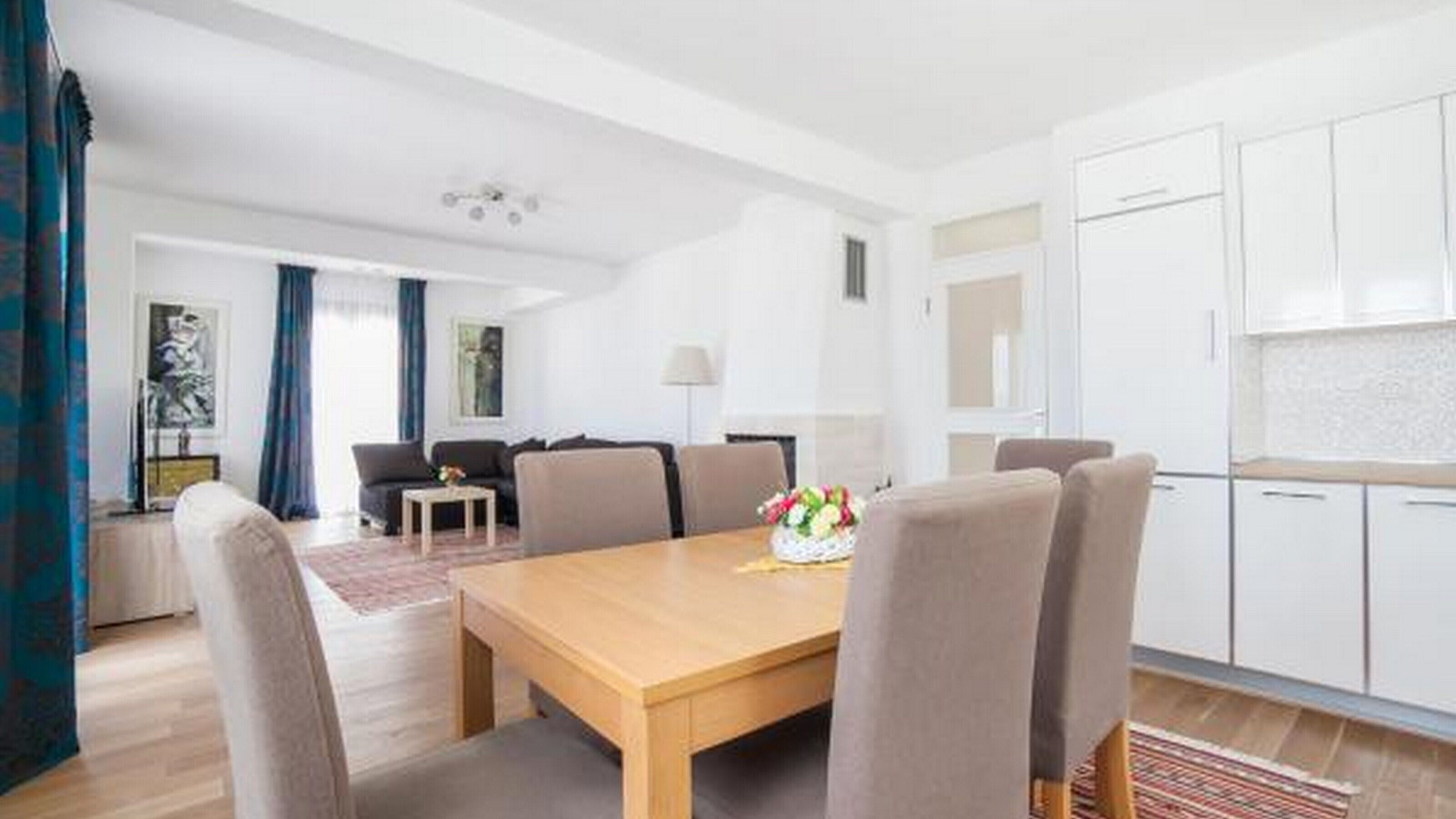 A modern living room with a sofa, coffee table, and a dining area with chairs and a table.