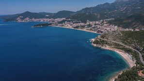 An aerial view of a coastal city with a long, curved coastline, dense urban development, and mountainous terrain in the background. - Apartments My Przno (Pržno)