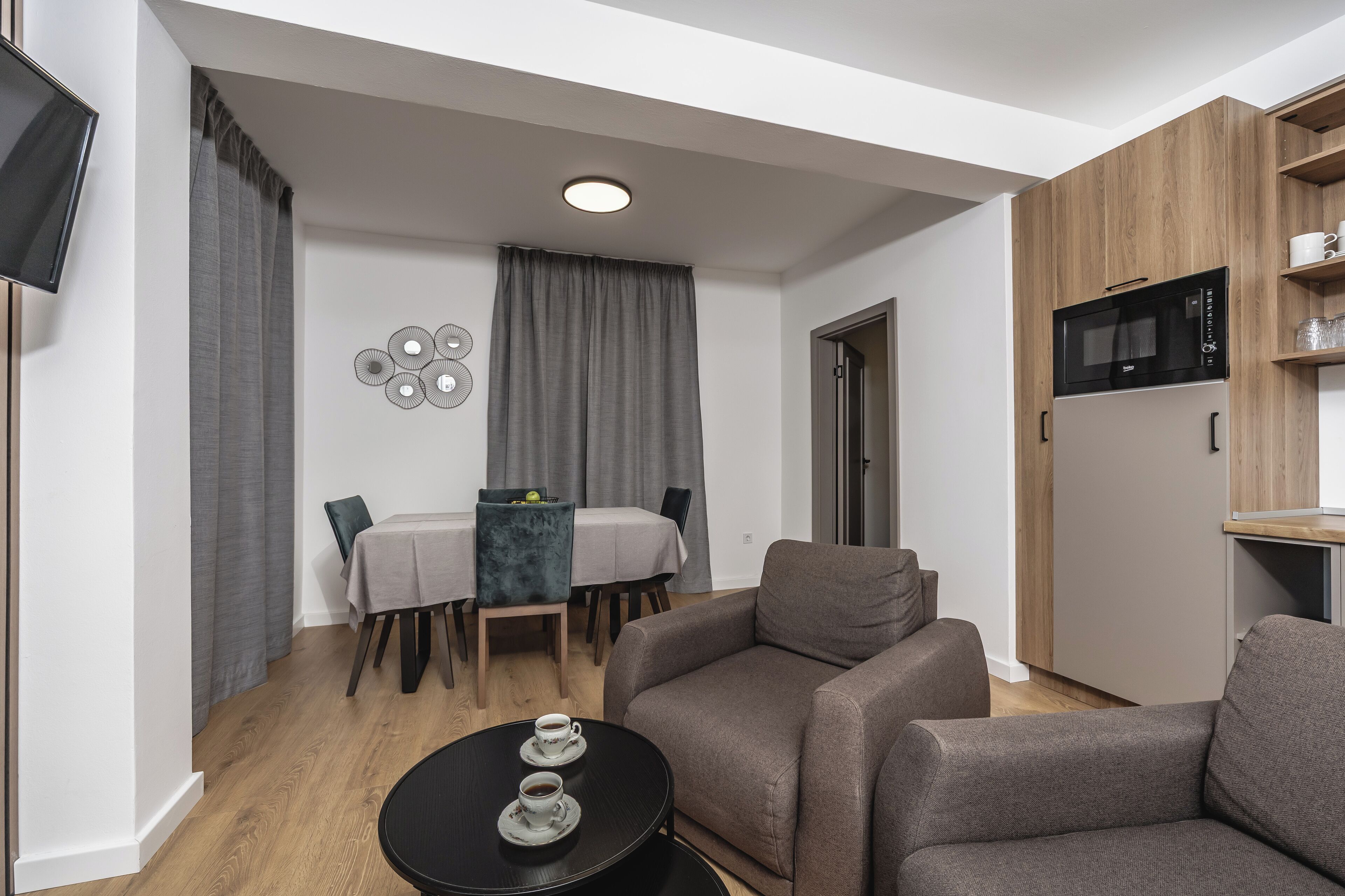 A modern living room with a sofa, a dining table with chairs, and a kitchen area with a microwave.