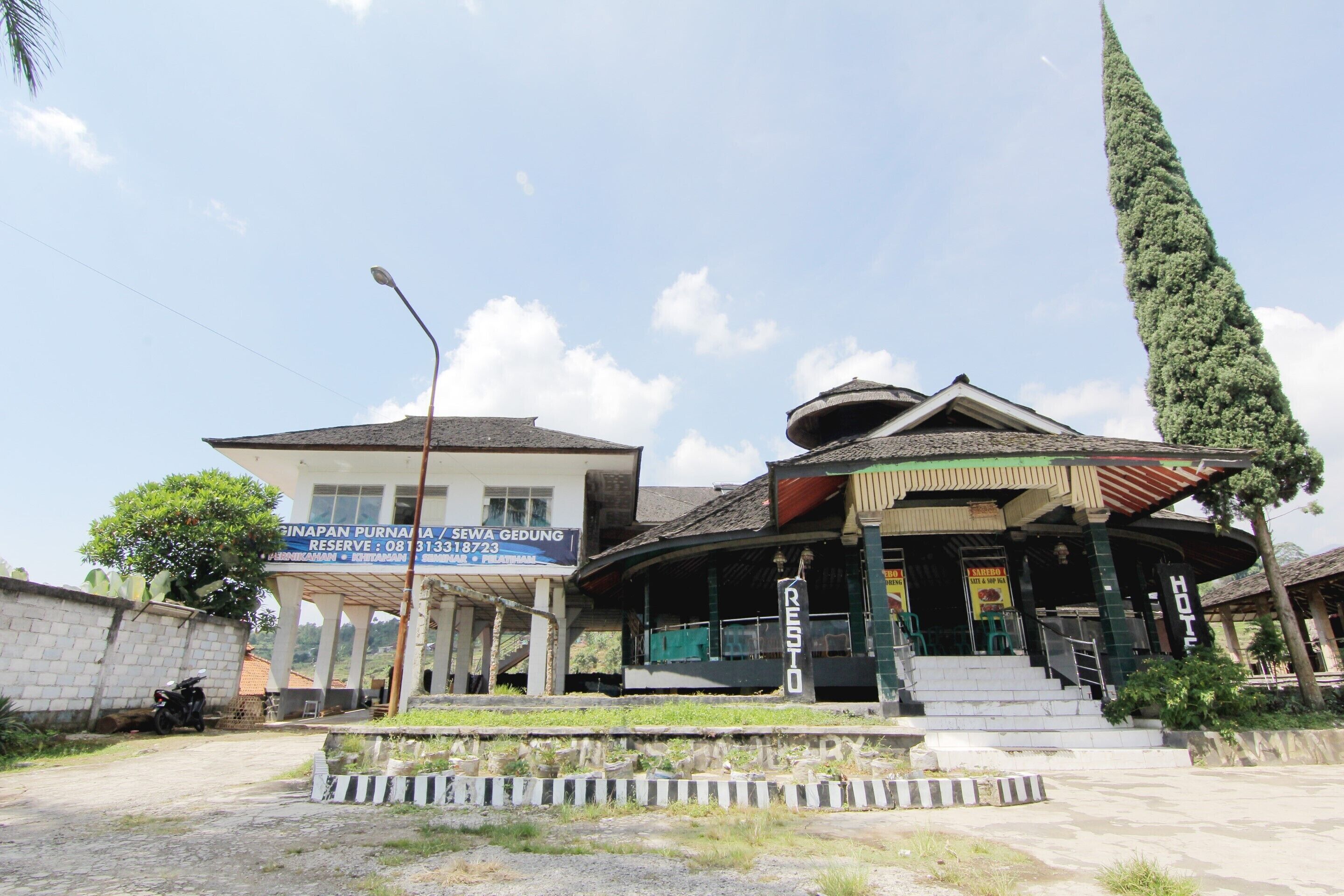 Un bâtiment portant une enseigne indiquant « Purnama Seva Gedung » et une autre enseigne indiquant « Resto », ce qui signifie qu’il s’agit d’un restaurant.