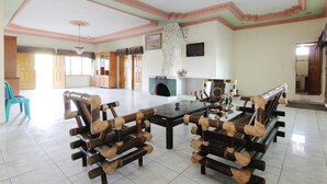 A spacious room with a large wooden dining table and chairs, a television mounted on the wall, and a fireplace.