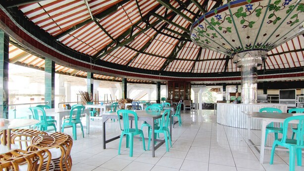 A spacious indoor area with tables and chairs, a tiled floor, and a high ceiling with a decorative element.