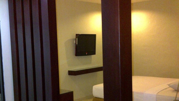 Une chambre d’hôtel avec un lit, un téléviseur fixé au mur et une cloison en bois.