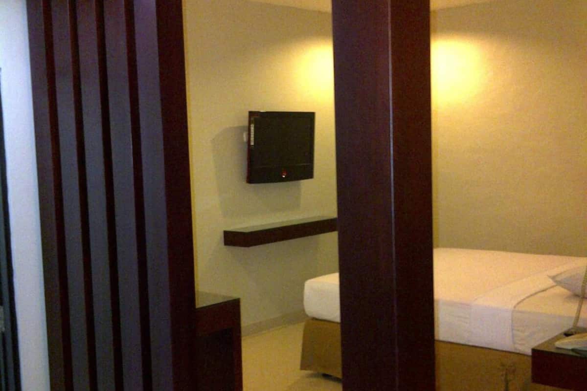 A hotel room with a bed, a TV mounted on the wall, and a wooden partition.