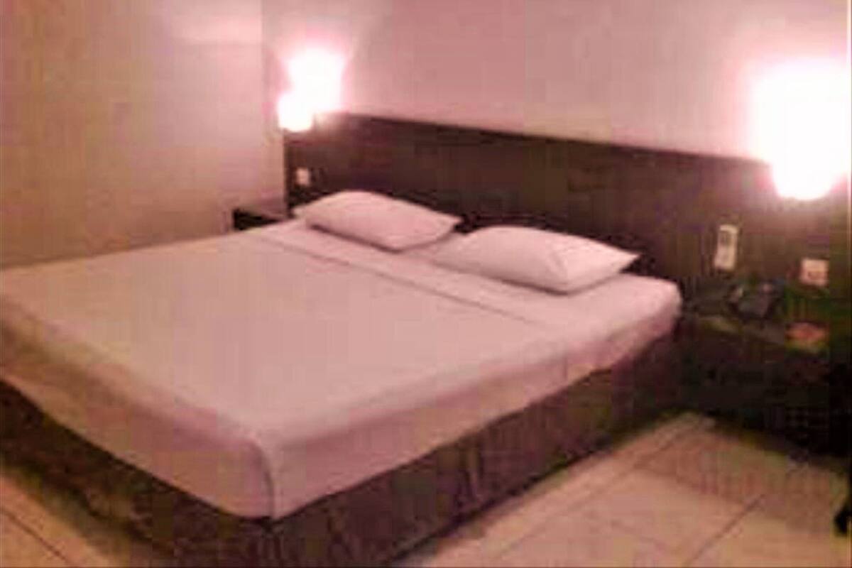 A standard hotel room with a single bed, a nightstand, and two wall-mounted lamps.