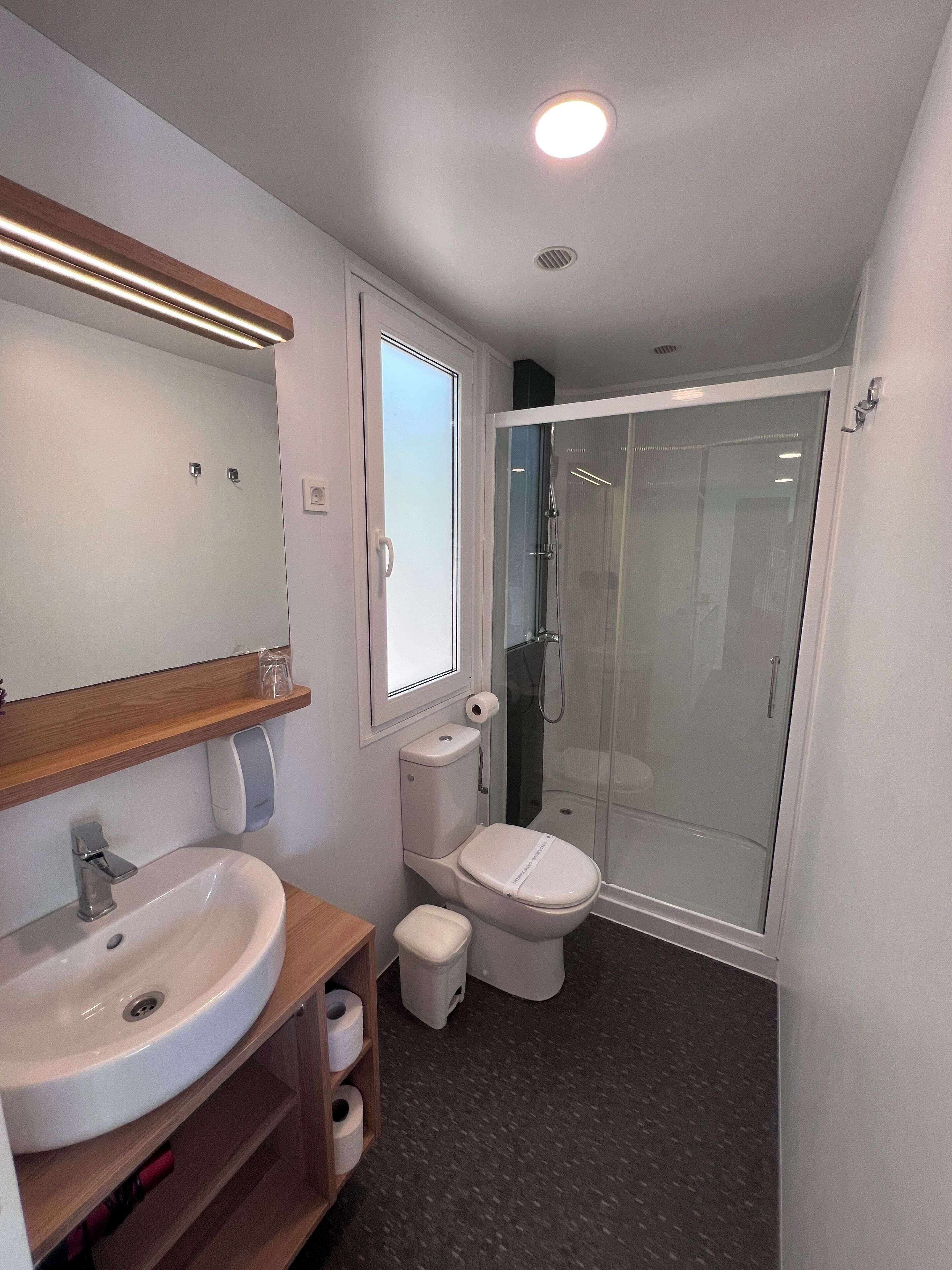 Een moderne badkamer met een wastafel, toilet en een douche met glazen wanden.