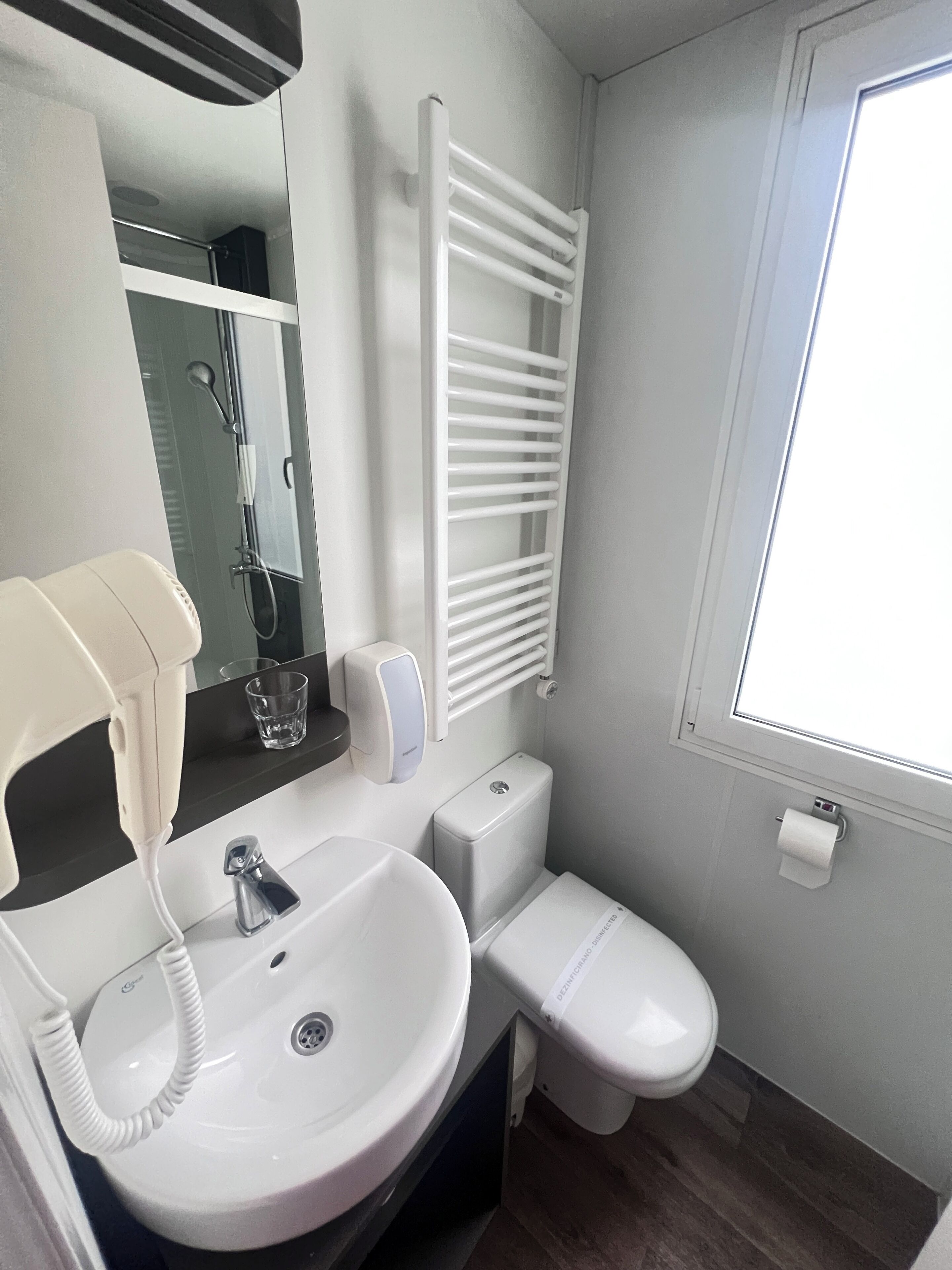 A bathroom with a white sink, a mirror, a towel rack, a toilet, and a window.