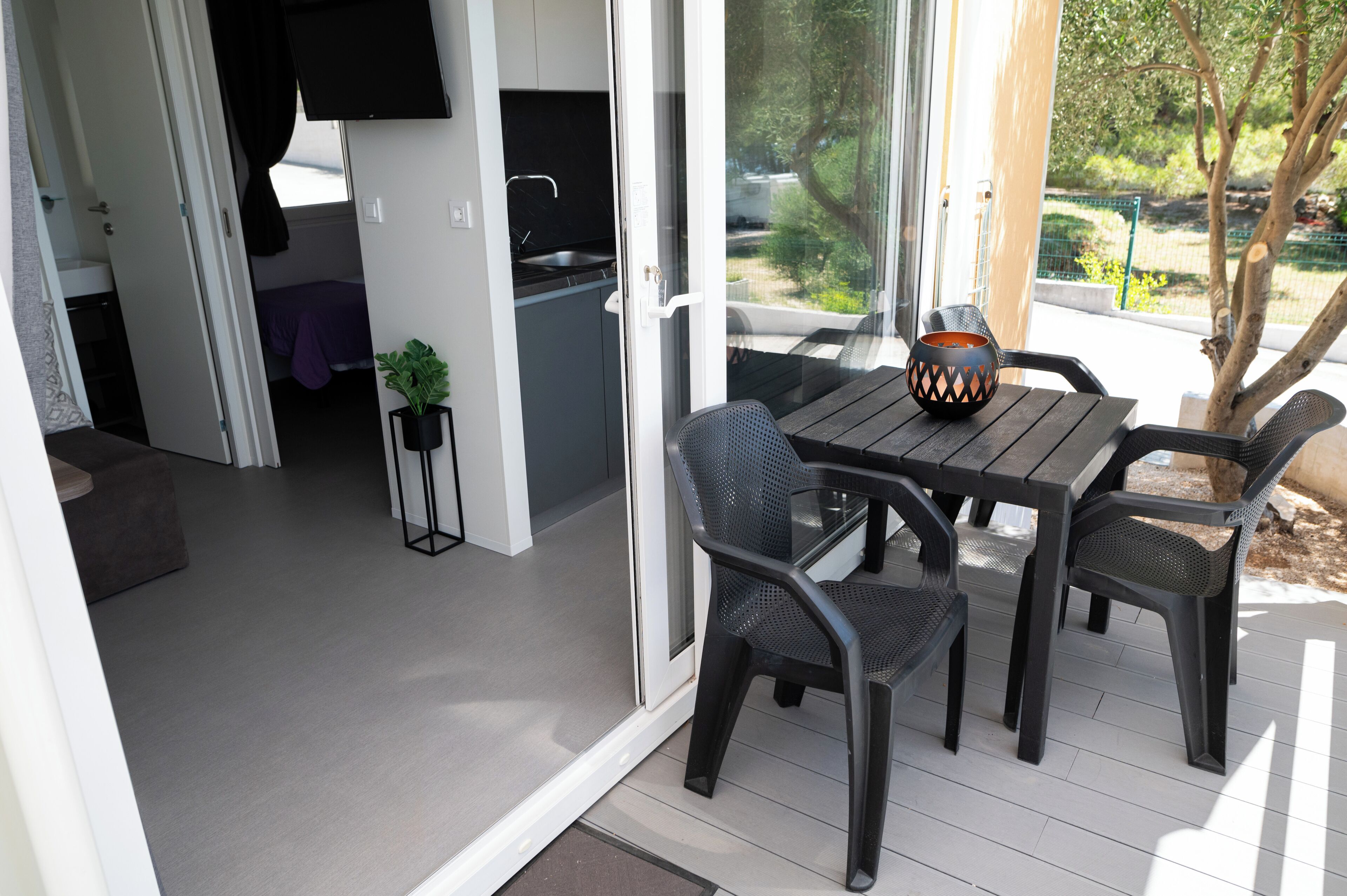 En patio med bord og stole, et lille tekøkken, samt en skydedør der fører til et udendørs område.