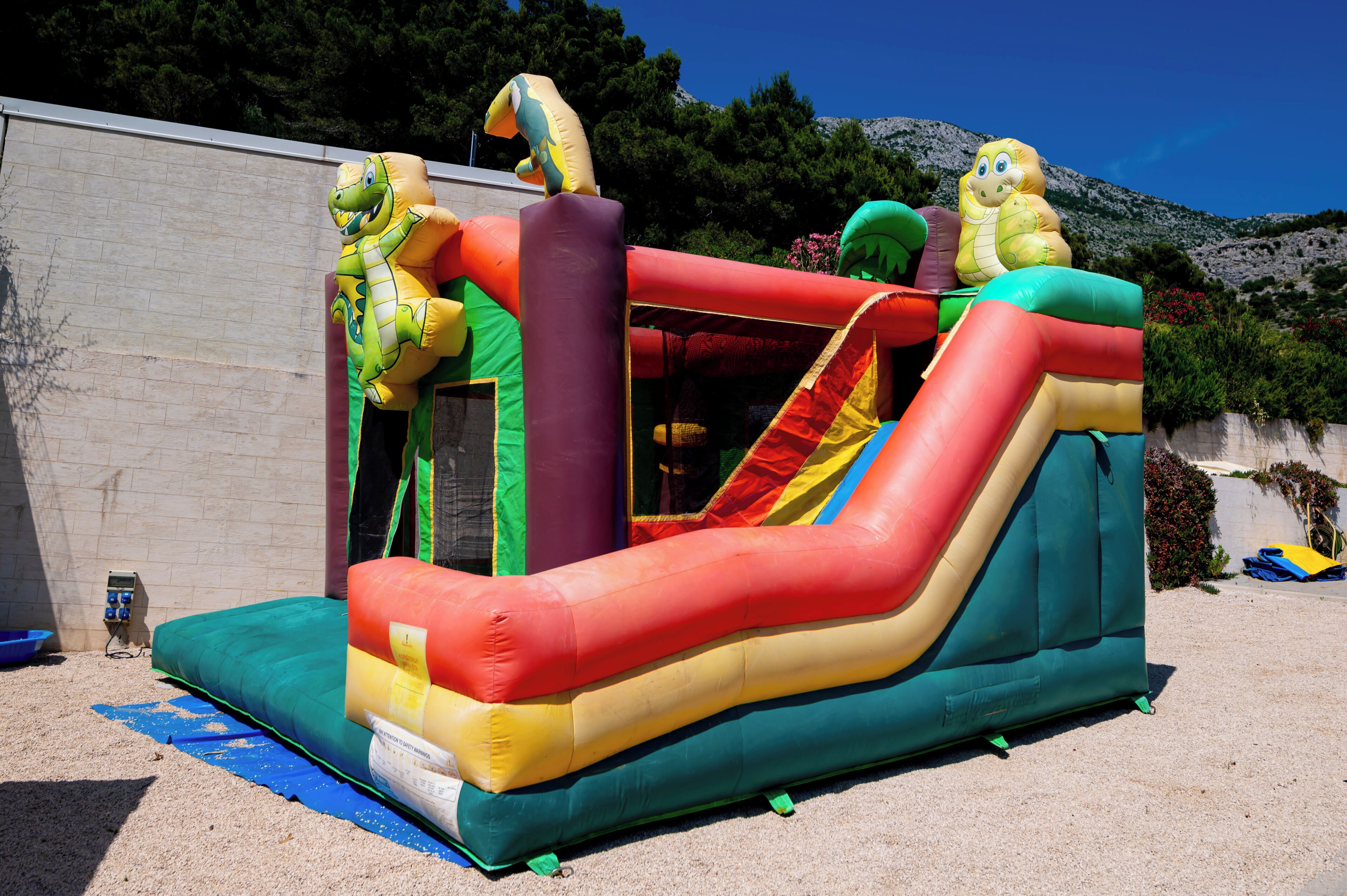 A colorful inflatable play structure with slides and climbing areas, set against a backdrop of trees and a clear sky.