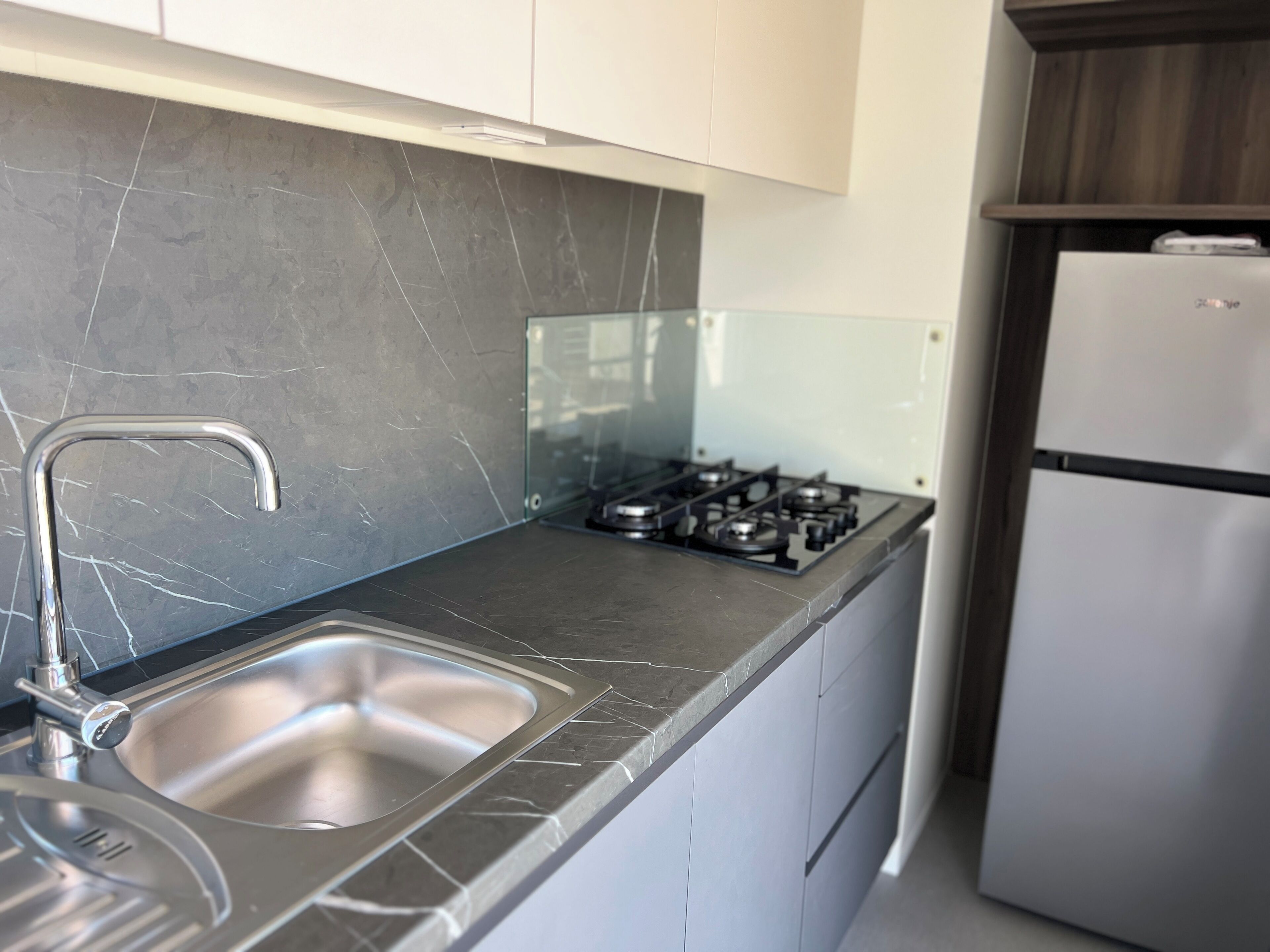 A modern kitchen with a stainless steel sink, a gas stove, and a white refrigerator.