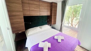 A bedroom with a bed, wooden headboard, and a window with a view of trees. - Camp Milo moje (Gradac)