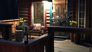 Een blokhut met een houten terras, een eethoek met stoelen en een tafel, en een raam met uitzicht op het omliggende bos.