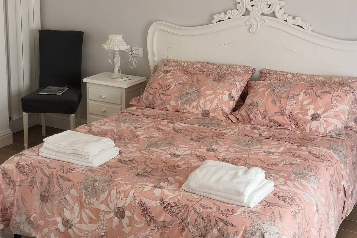 Ein ordentlich bezogenes Bett mit Blumenmuster, ein weißer Kopfteil und ein Chandelier.